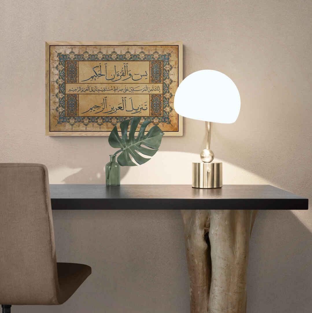 Surah Yasin canvas wall art in gold and blue calligraphy on a wooden desk with a plant and notebook.