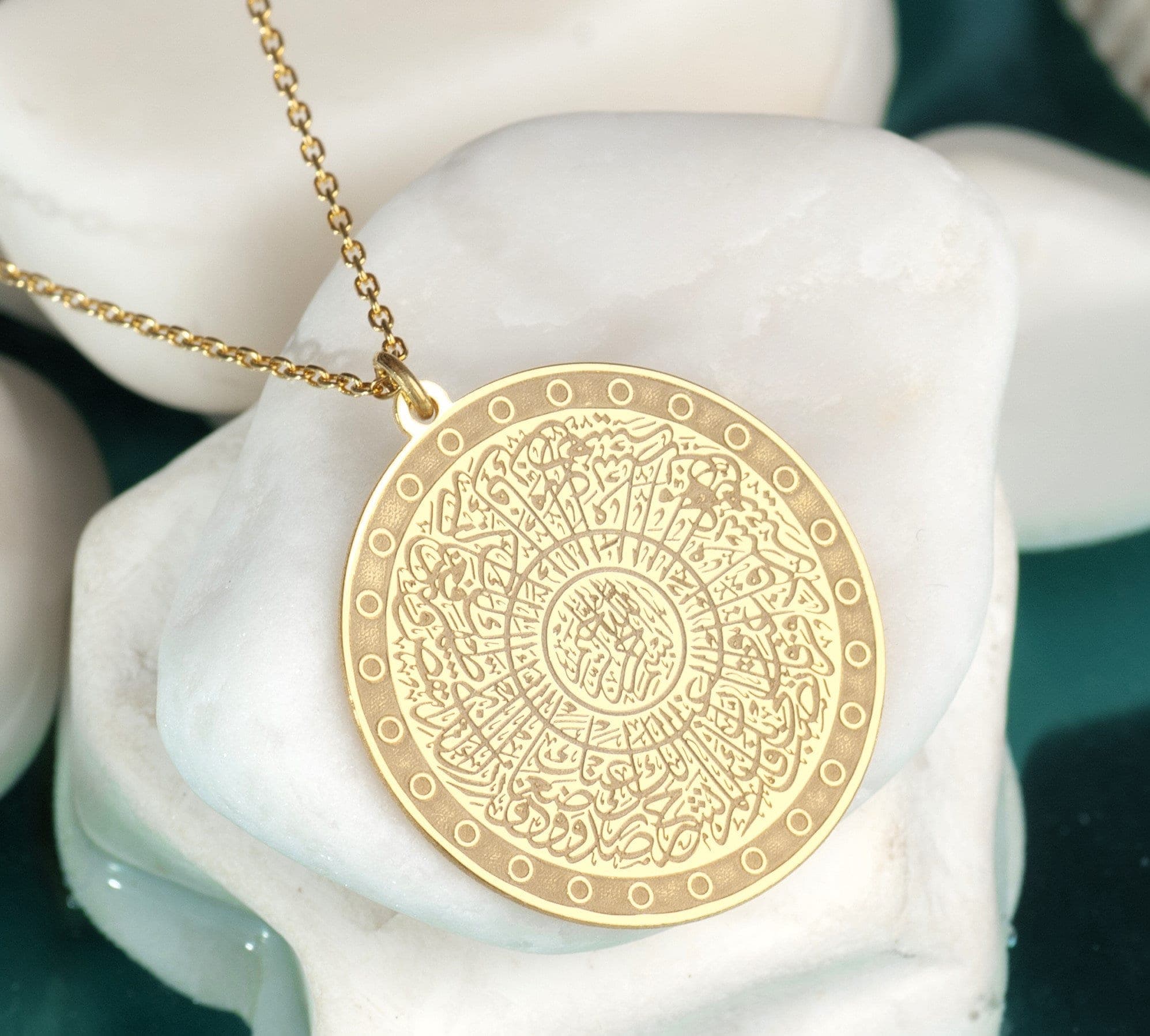 Surah Inshirah Necklace Necklace written can be worn every day. It is made by hand in our workshop with care. All our jewelry is the most elegant choice for the bridesmaids, friends, your loved ones and for yourself. It is also a fact that silver jewelry improves blood circulation and provides electricity and makes you feel awake. A gold necklace with a round pendant featuring intricate Arabic calligraphy in a circular pattern. The pendant is surrounded by a decorative border of small circles.