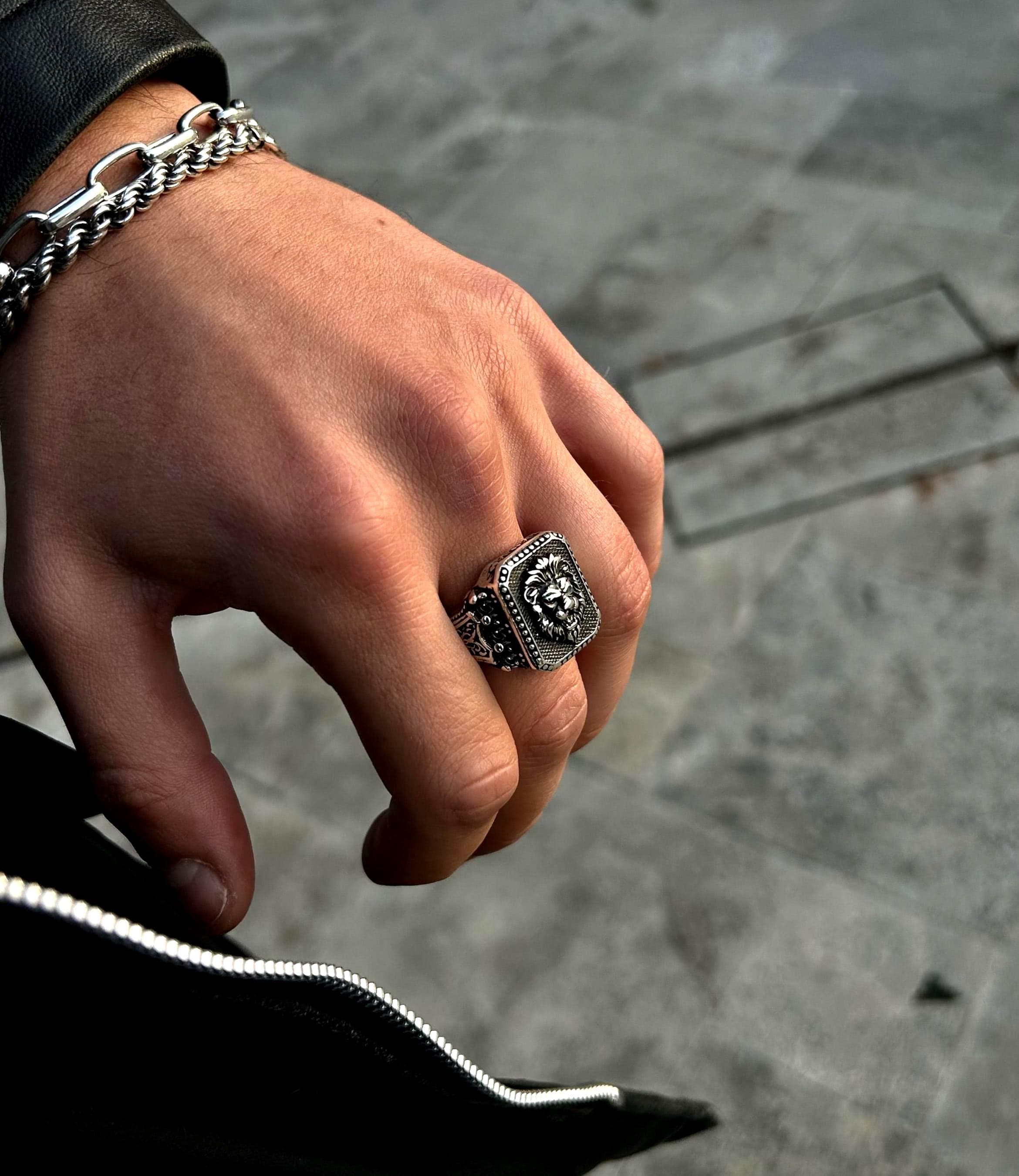 A man's hand wearing a bold, handmade 925 sterling silver lion head statement ring with detailed craftsmanship against a black leather jacket.