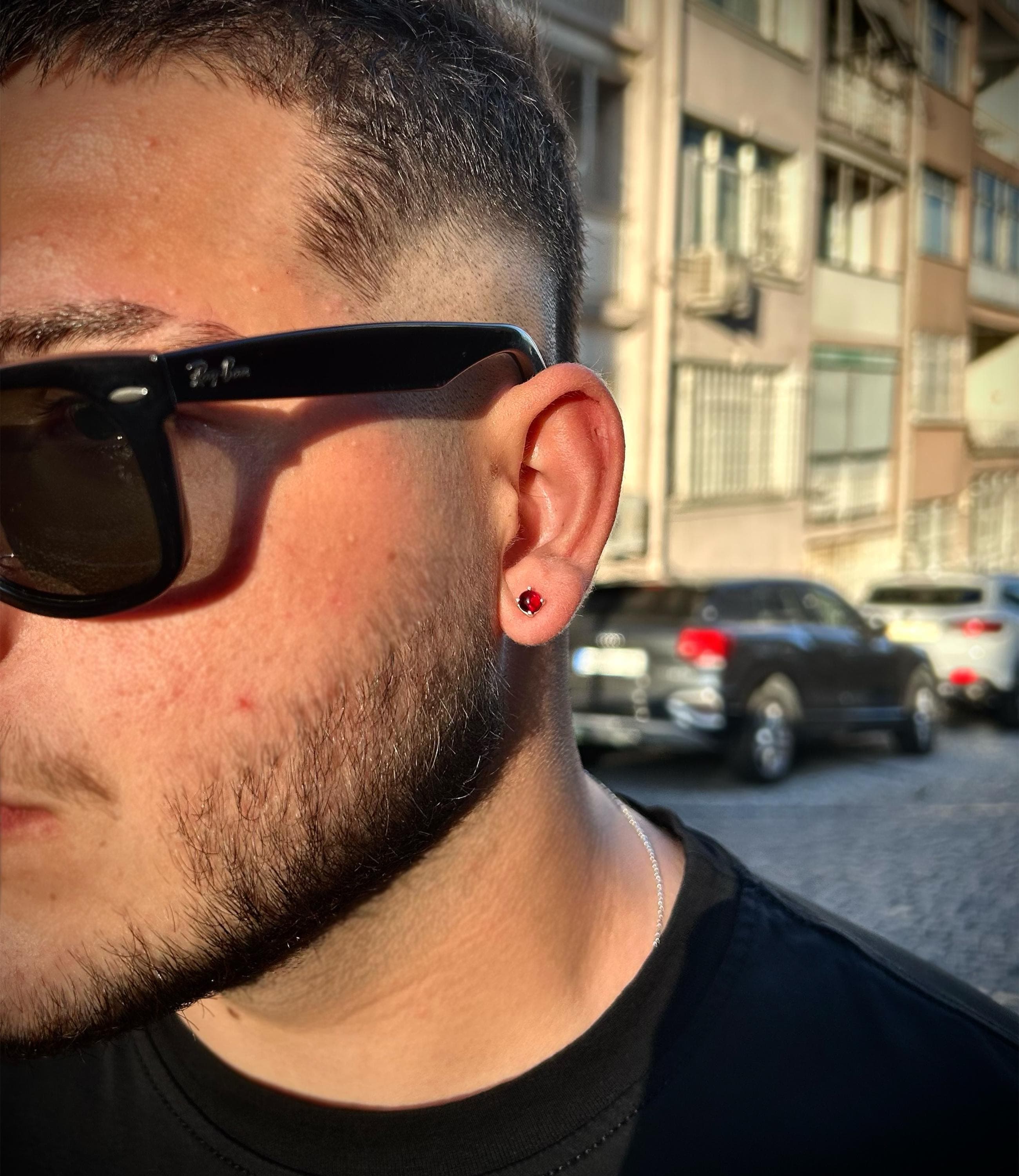 Burgundy stud earring for men made of 925 sterling silver, photographed on neutral fabric with warm light to highlight its deep red color tone, minimalist and bold.