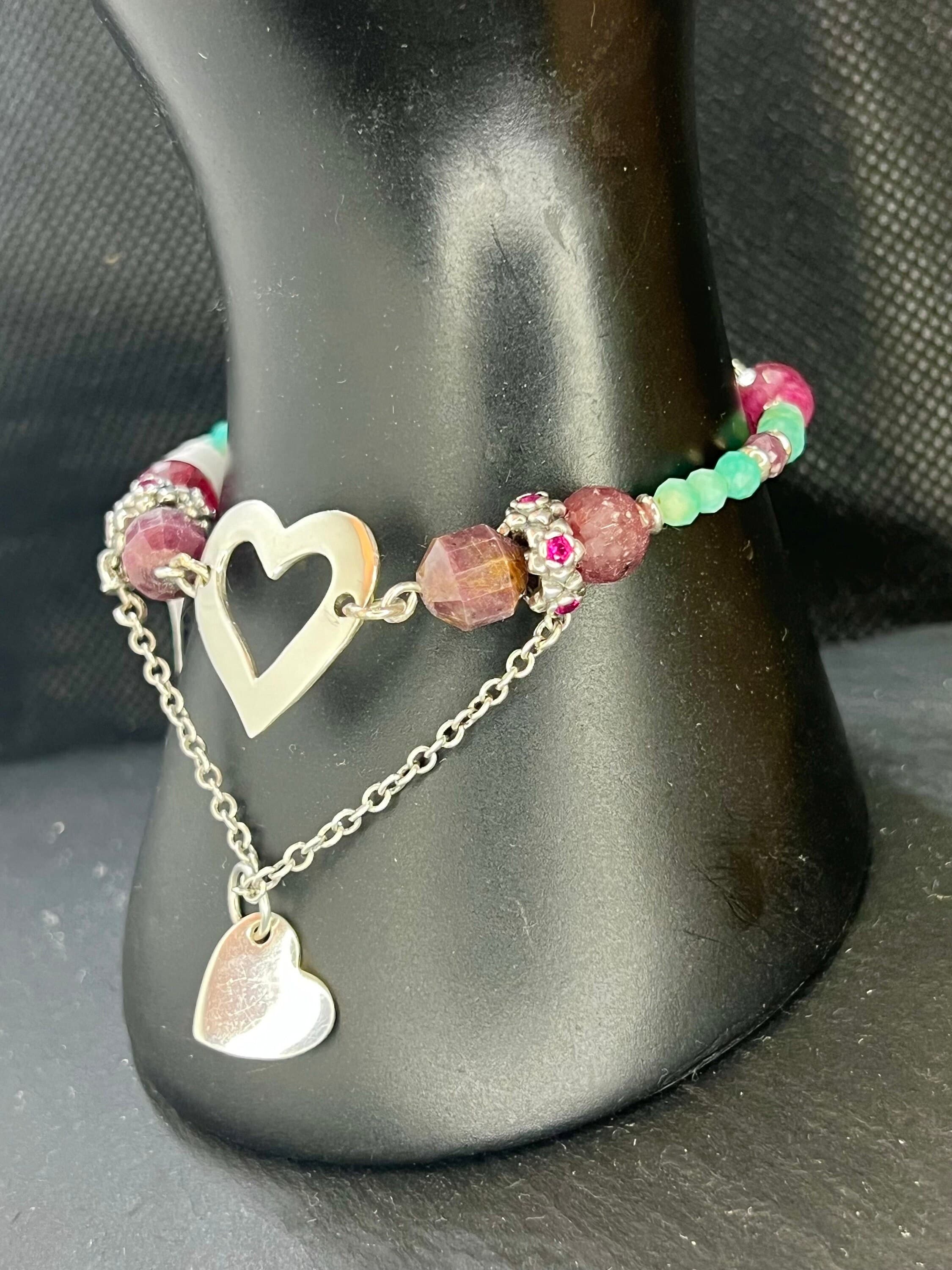 A silver charm bracelet with a heart-shaped charm and a chain with a smaller heart charm. The bracelet is made with pink and turquoise colour beads.