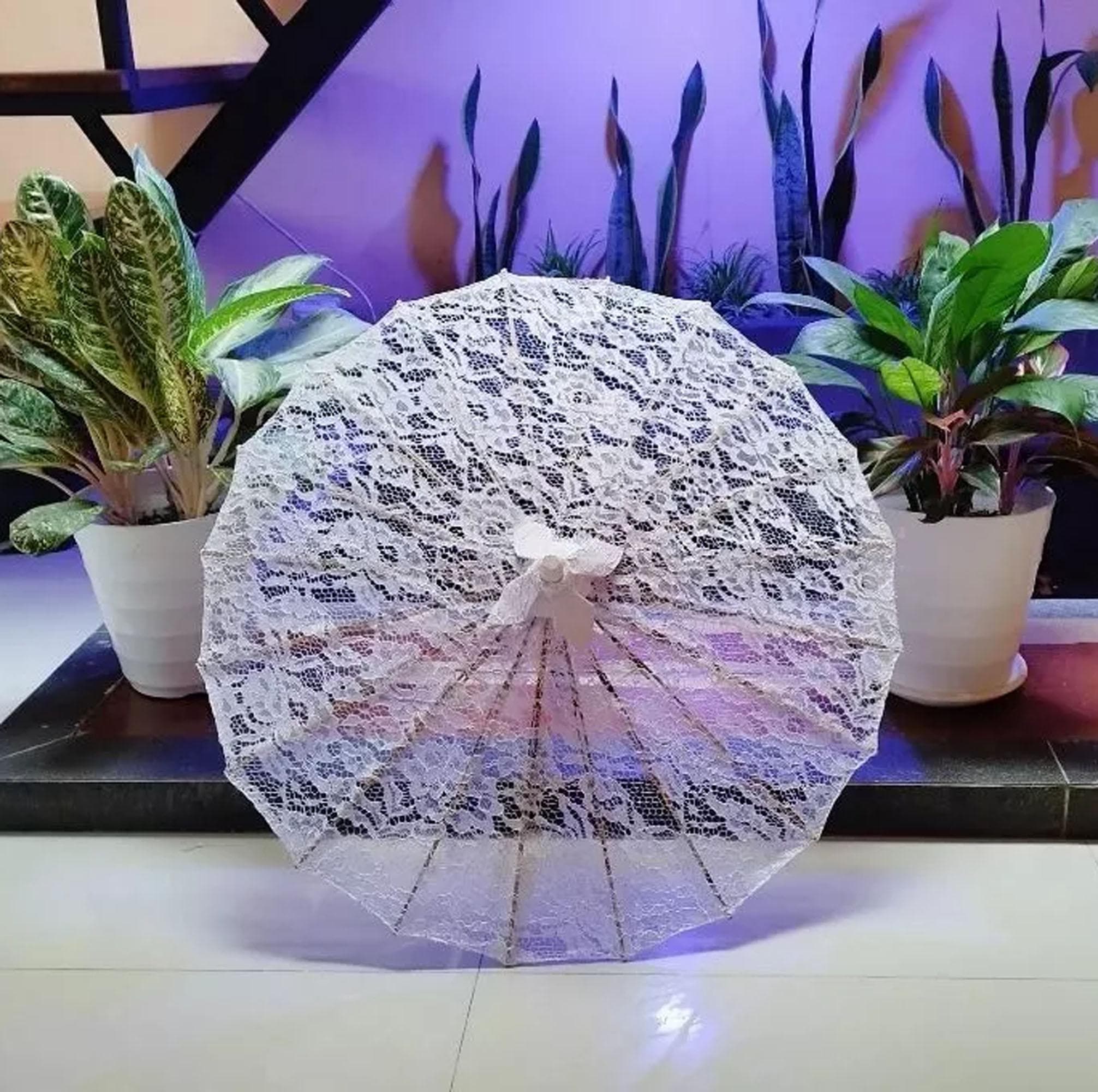 White lace parasol with wooden handle displayed open on grass, showing floral lace pattern and bamboo frame.