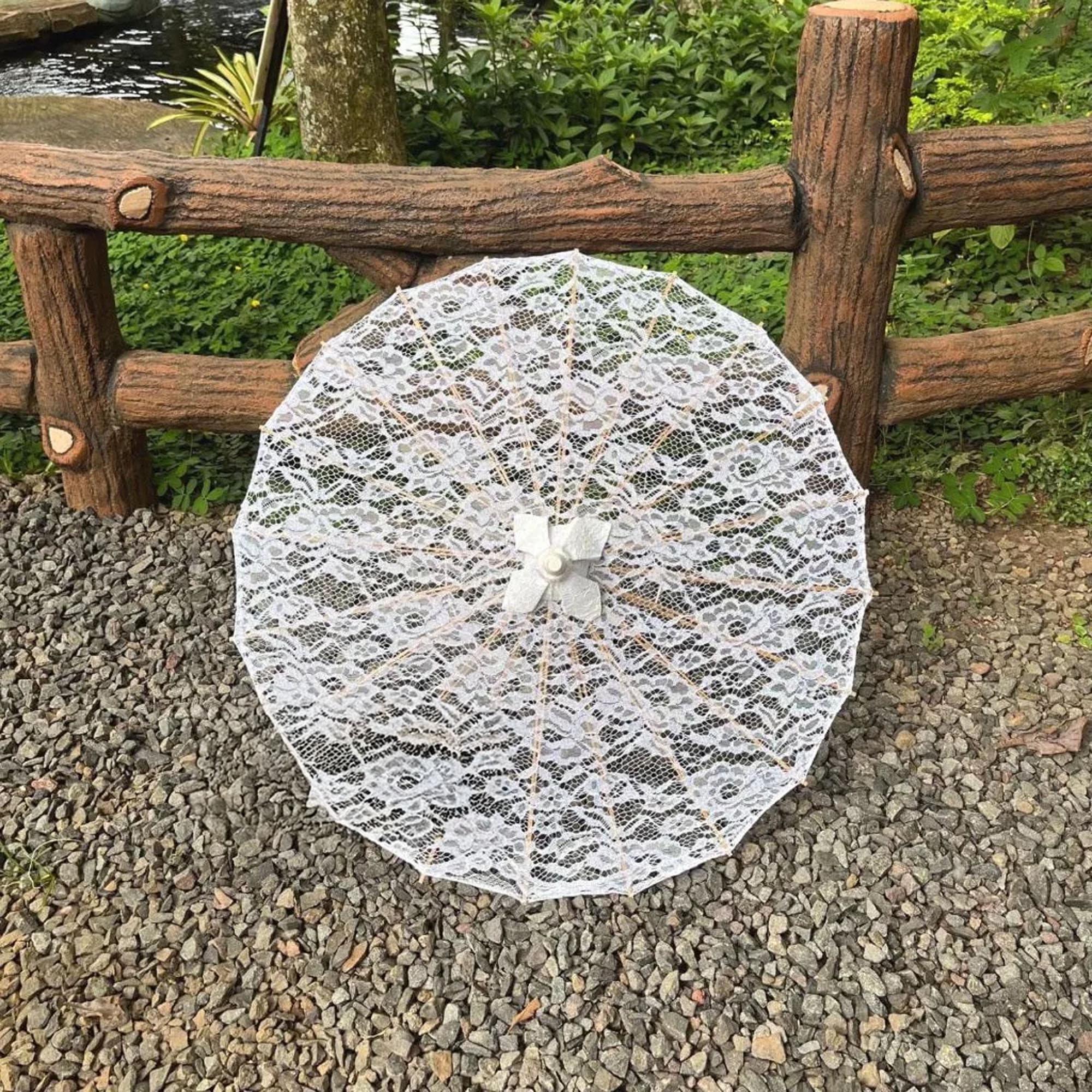 White lace parasol with wooden handle displayed open on grass, showing floral lace pattern and bamboo frame.