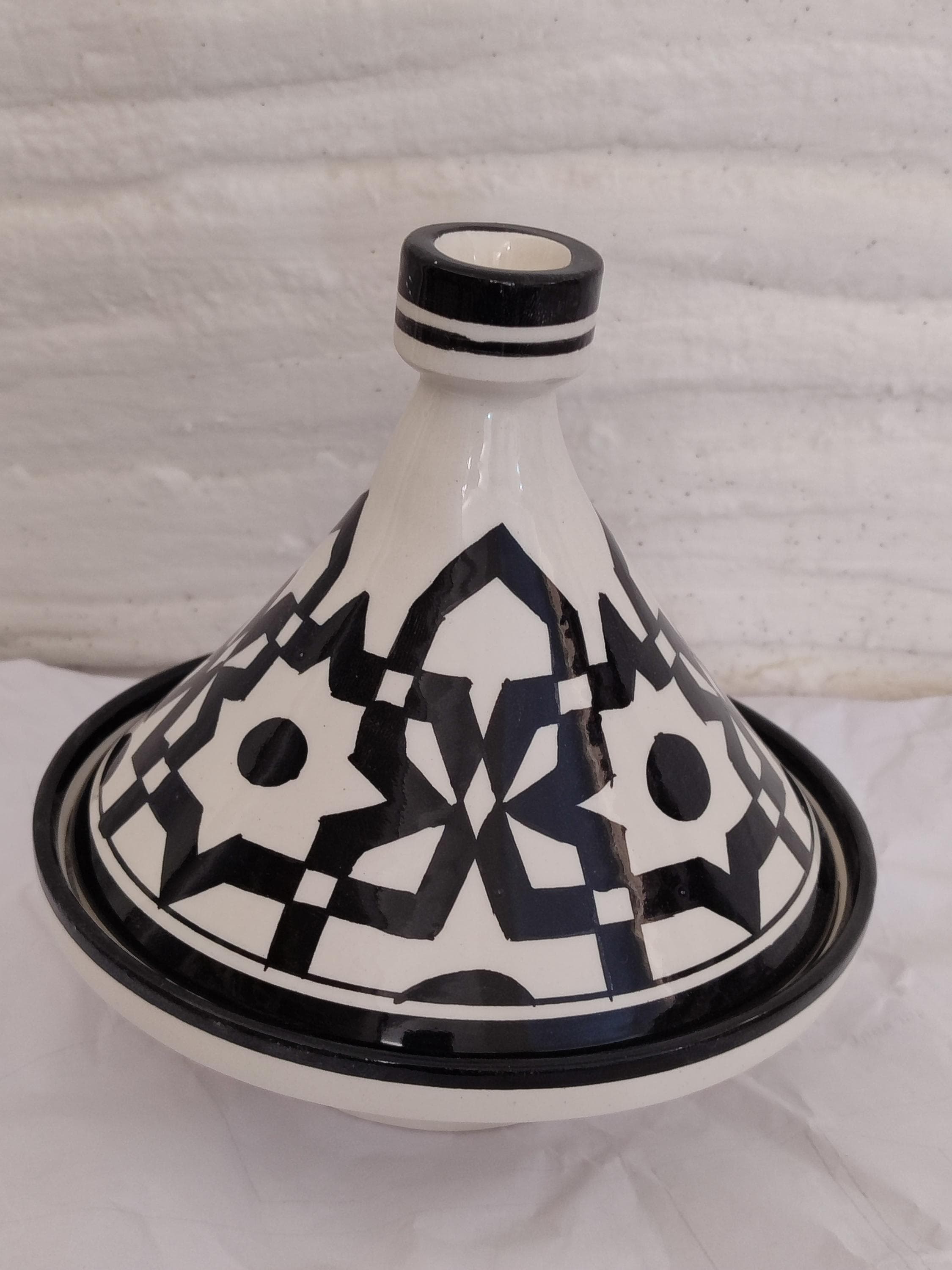 Cook like in Marrakech with this artisanal tajine / Kochtajine, handmade from clay / Ton using age-old Moroccan techniques. This unique tajine / einzigartiger Schmortopf allows flavors to blend slowly while the conical lid / kegelförmiger Deckel retains moisture. The black and white ceramic finish / Keramikdekor pays tribute to Fez pottery art / Töpferkunst aus Fès. Perfect for tagine enthusiasts / Tajine-Liebhaber and fans of traditional North African cooking / nordafrikanisches Kochen.