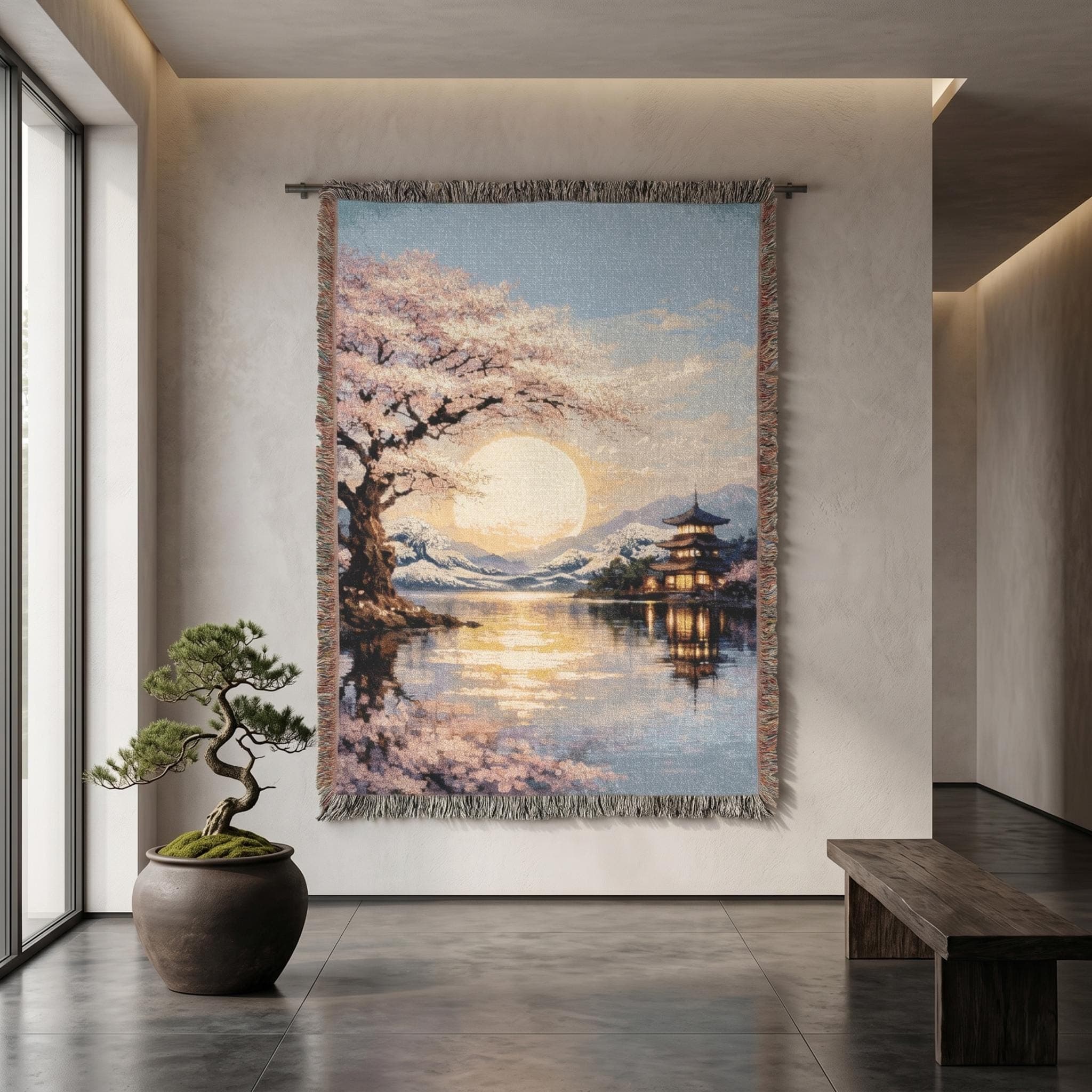 Woven tapestry wall hanging featuring a serene Japanese inspired lakeside scene with a blooming cherry blossom tree, a glowing sunset sun, calm reflective water, a lit pagoda, distant snowy mountains, and soft pink blossoms along the shore. Scenic sakura wall art with peaceful zen decor mood and warm evening light, ideal as a large wall tapestry, decorative throw blanket, bedroom accent, and gift for cherry blossom lovers, Japan decor fans, and tranquil landscape collectors.