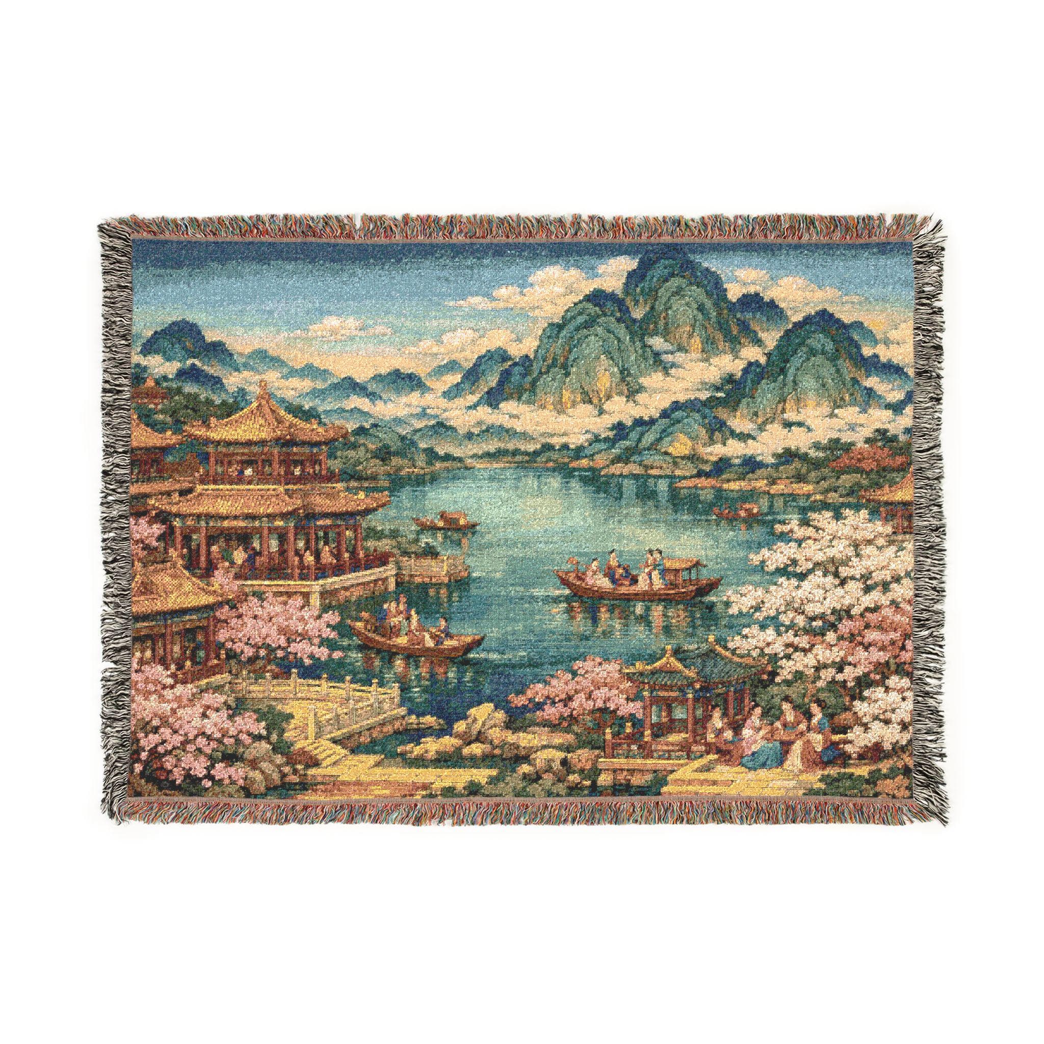 Woven tapestry wall hanging with fringe edges showing an East Asian lakeside scene: golden pagodas and pavilions, pink cherry blossoms, small boats on tranquil water, and misty mountains under a bright sky. Rich woven texture gives a vintage wall art look, perfect for living room, bedroom, entryway, or meditation nook. Also works as a cozy woven throw blanket. Ideal for Asian inspired decor, chinoiserie style, zen home decor, and spring sakura lovers. Gift for travelers and nature lovers.