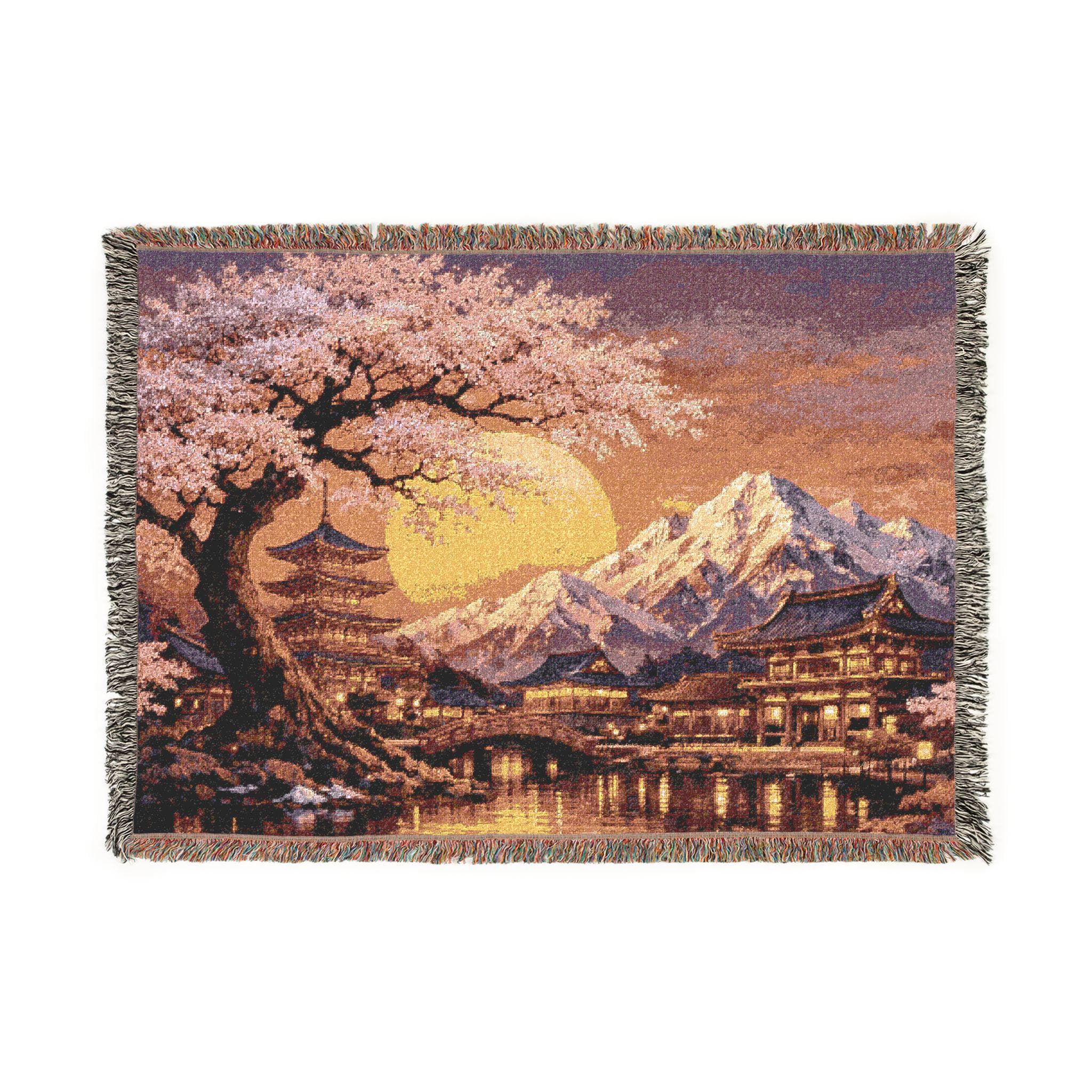 Woven tapestry wall hanging featuring a glowing cherry blossom sunset with pink sakura tree, Japanese temple buildings, pagoda, bridge, reflective water, and snowcapped mountains in the background. Asian landscape decor in warm peach, gold, lavender, and deep blue tones with rich woven texture and fringe. Perfect for bedroom, living room, reading nook, meditation room, or as a woven throw blanket. Ideal gift for sakura lovers, Japan decor fans, and peaceful nature-inspired home styling.